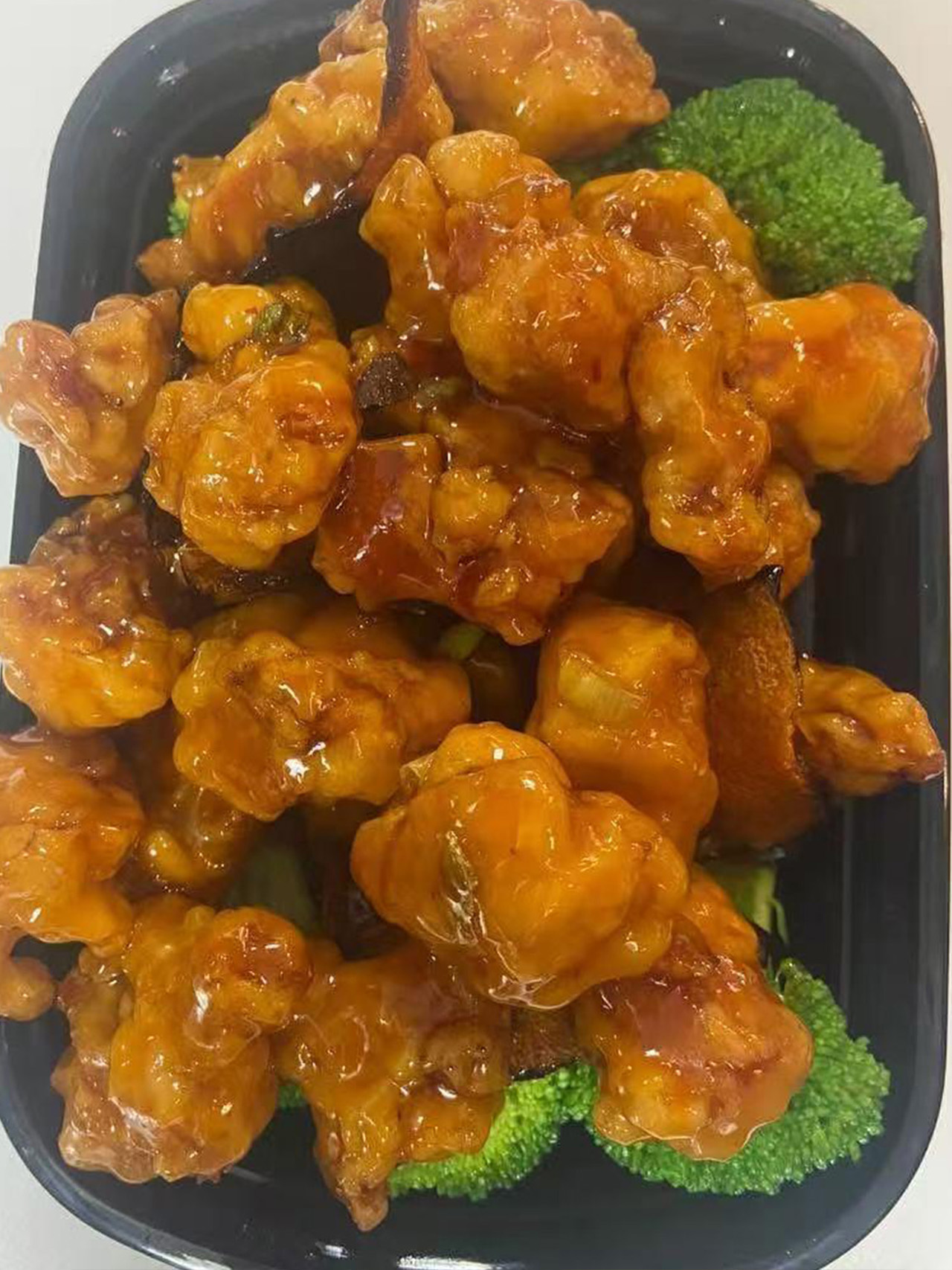 Glazed orange chicken with broccoli in a takeout box.