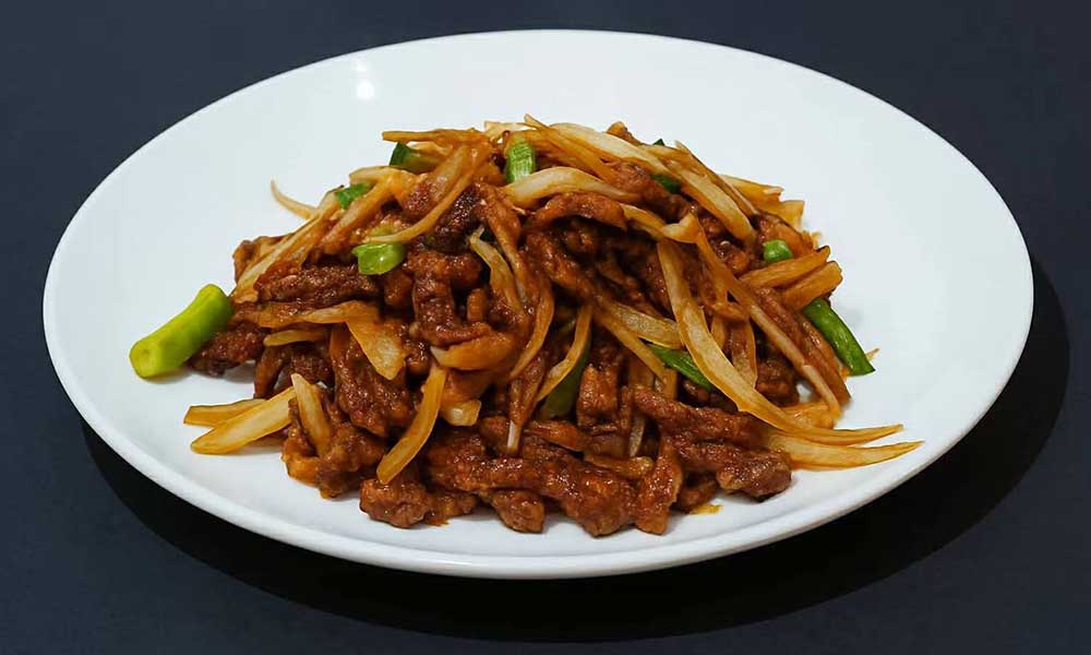 Savory stir‑fried beef shreds mixed with sliced white onion and green scallion segments, coated in brown sauce, arranged on simple white ceramic plate.