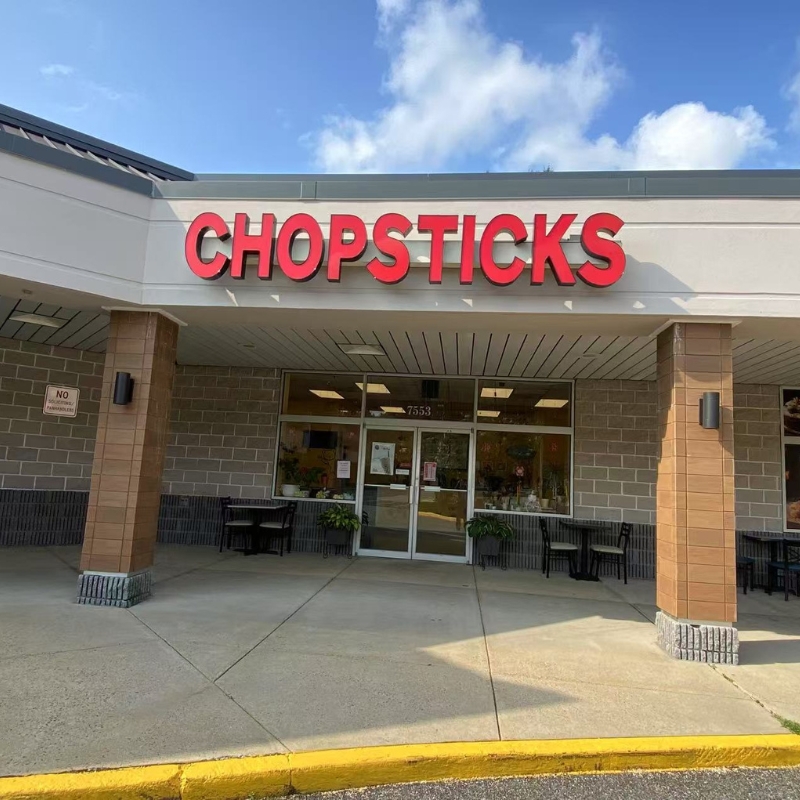 Exterior of Chopsticks Express, brick - walled, with red signage and outdoor seating.