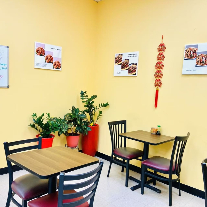 Square table area in Chopsticks Express, yellow walls, plants, and red - cushioned chairs.