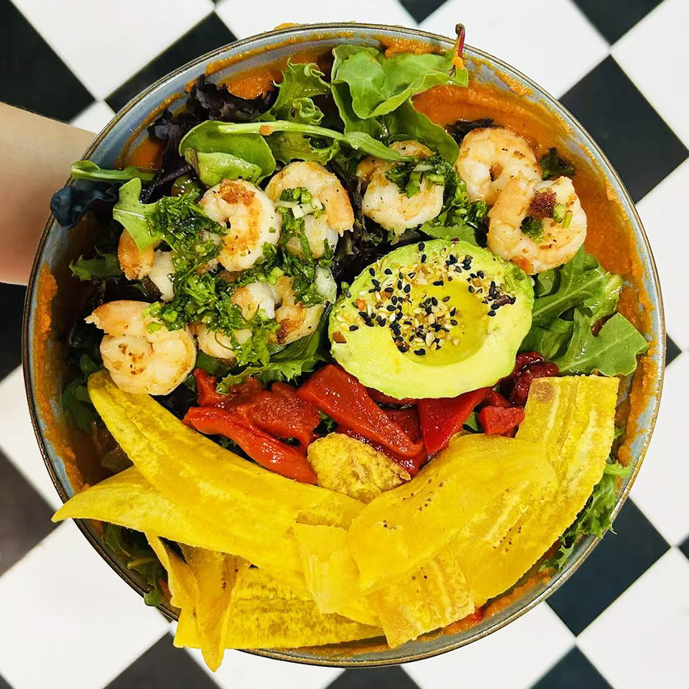 Colorful bowl with grilled shrimp, fried plantains, avocado, and greens at Costa，a Colombian Restaurant in Houston