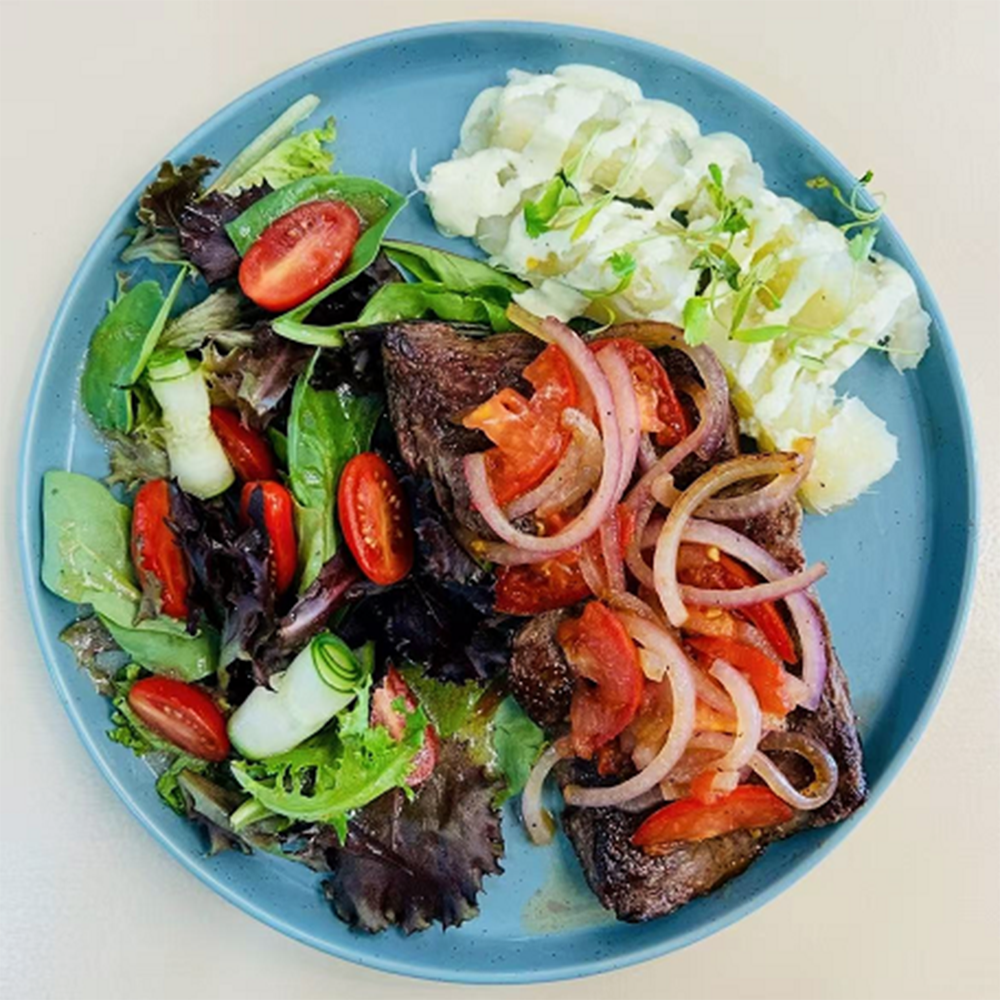 Plate of grilled steak with onions, mashed potatoes, and fresh side salad at Costa，a Colombian Restaurant in Houston