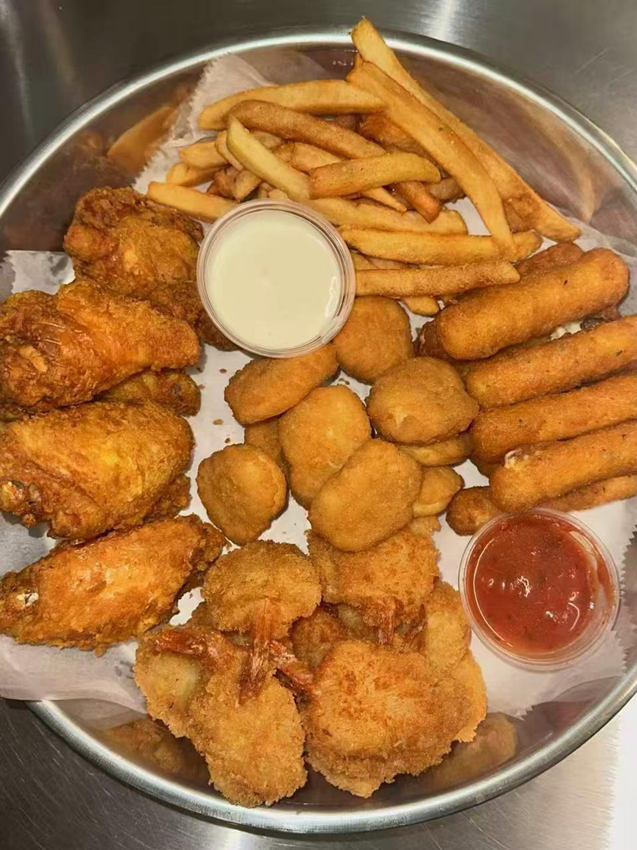 Fried platter with chicken wings, shrimp, fries, and dipping sauces on a metal tray