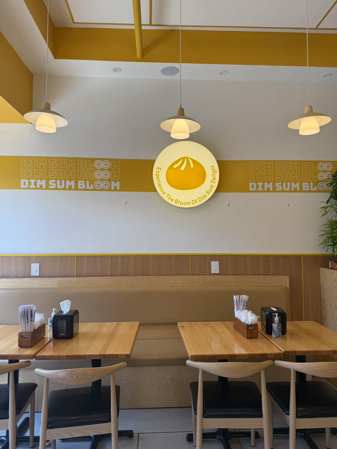 Bright dining hall with signature dumpling logo and warm yellow accents at Dim Sum Bloom Rockville Centre, a Chinese Restaurant in Rockville Centre
