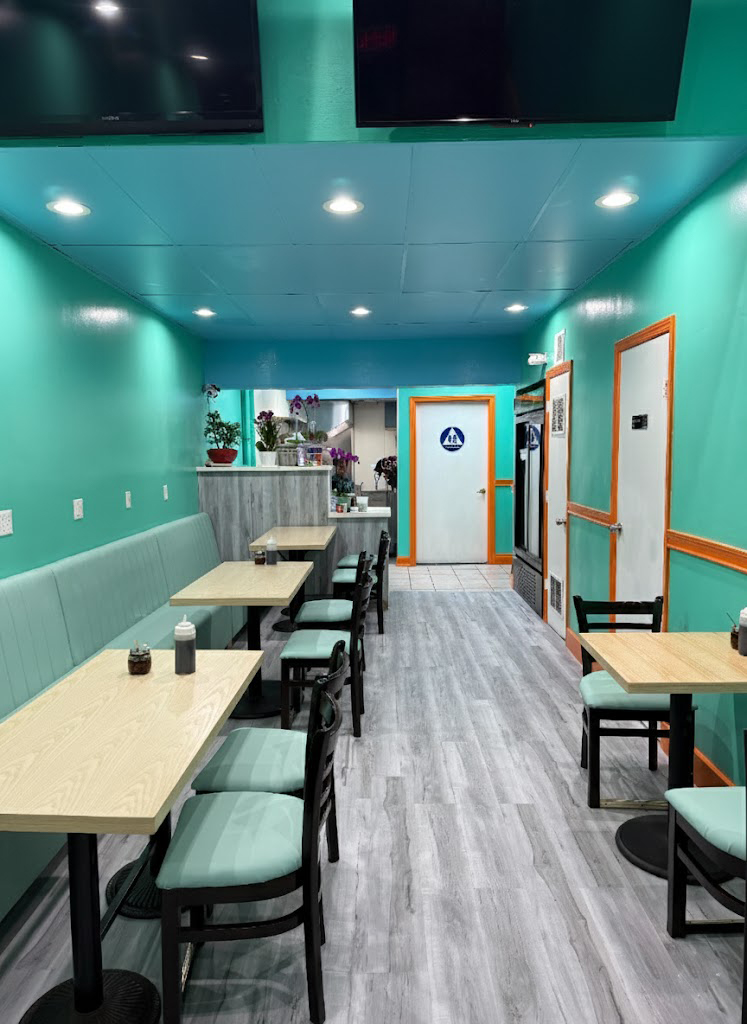 Bright modern restaurant with turquoise walls, wood tables, booths, and ceiling-mounted TVs.