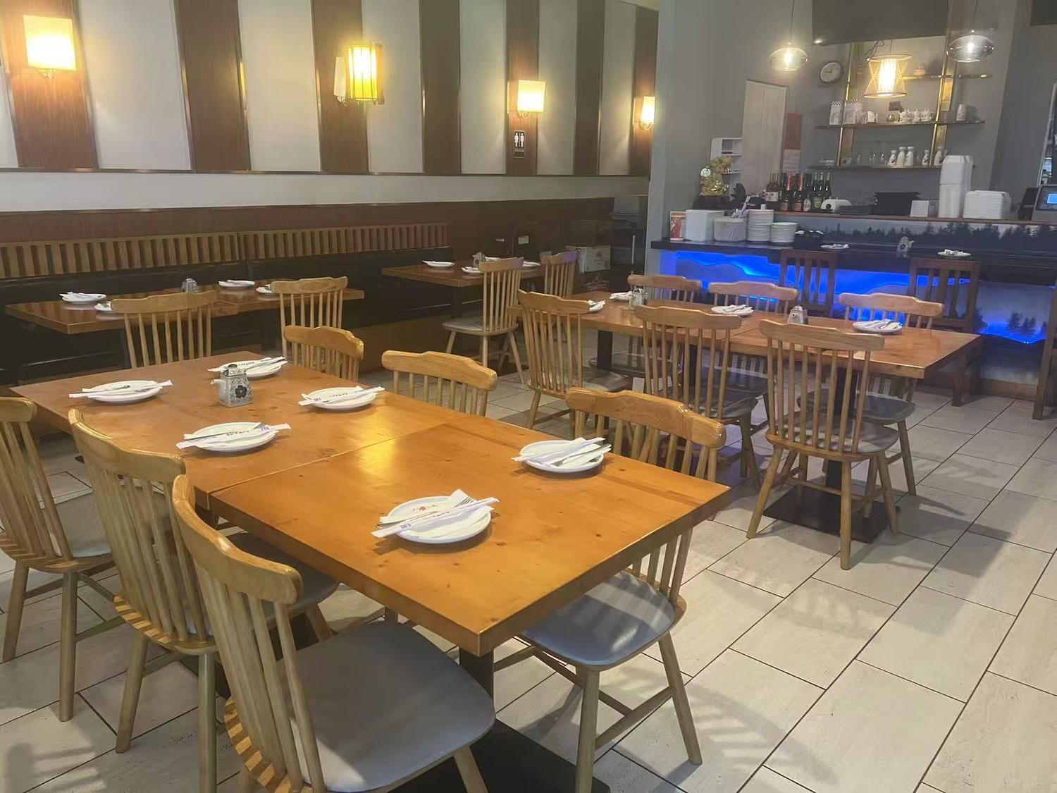 Interior of a casual Asian restaurant with wooden tables and chairs, booth seating along the wall, and a bar counter with blue under-lighting.