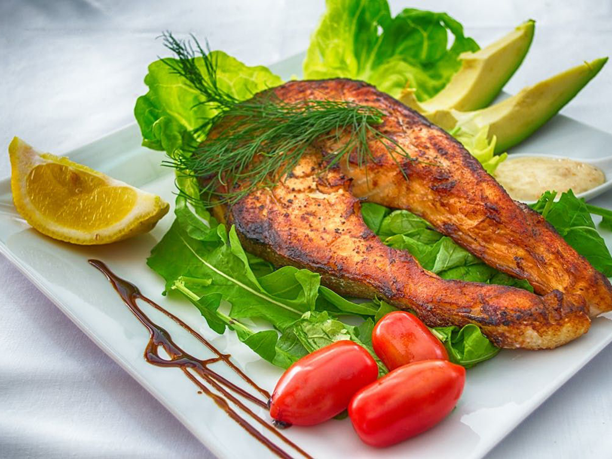 Grilled salmon steak with fresh greens, tomatoes, and lemon at Ditan Er BBQ, a Barbecue restaurant in Flushing