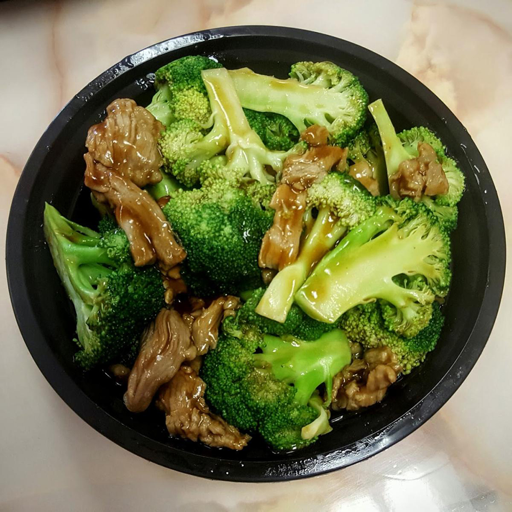 Black plastic bowl filled with stir-fried beef and broccoli, coated in glossy brown sauce, classic American Chinese takeout dish.