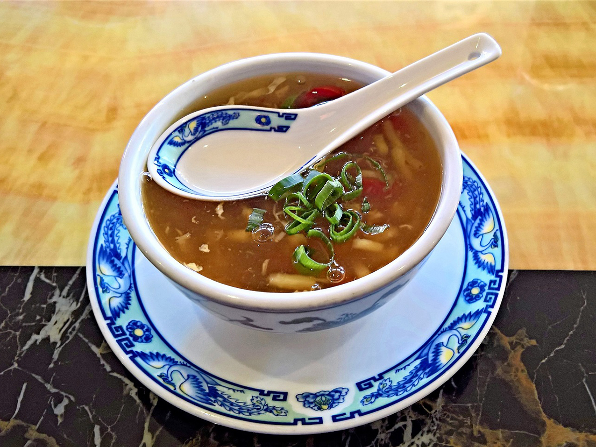 Hot sour soup garnished with chopped green onions in blue patterned ceramic bowl at Dragon Inn, a Chinese Restaurant in Fredericksburg