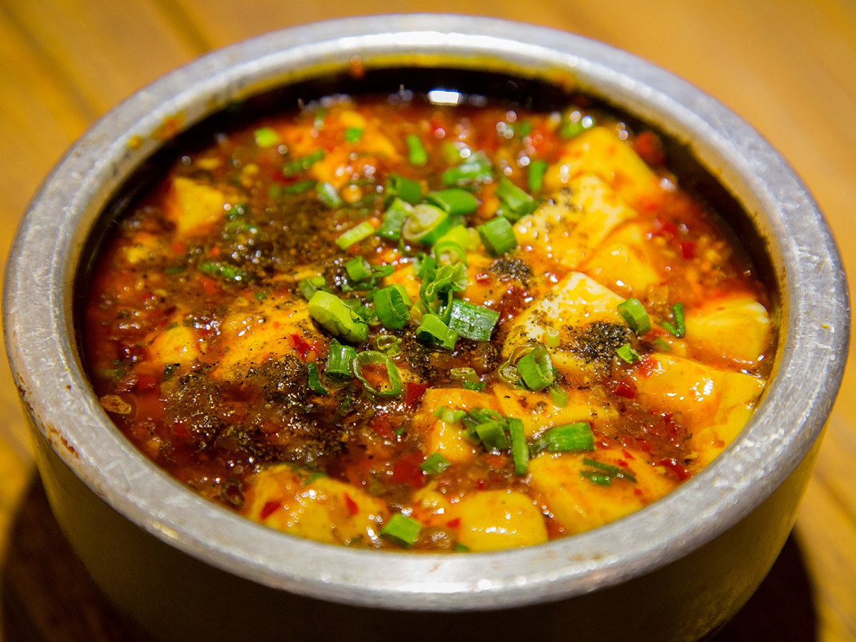 Spicy mapo tofu topped with chopped scallions served in a metal pot at Dragon Inn, a Chinese Restaurant in Fredericksburg