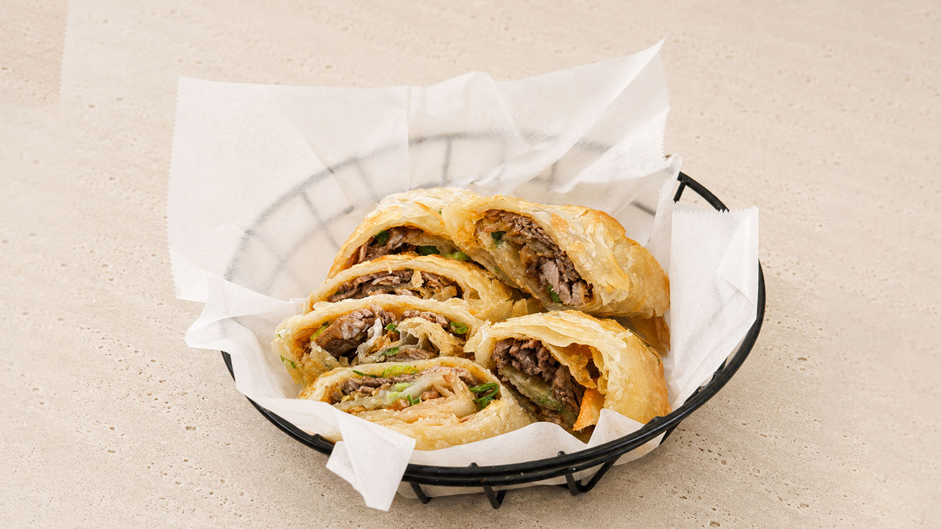 Beef and scallion pancakes cut into pieces, served in a black basket with paper