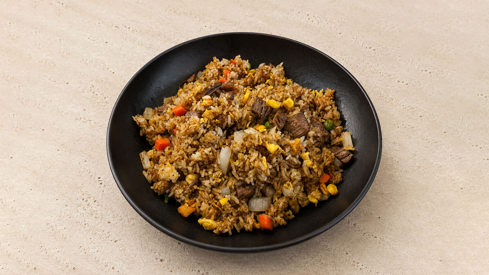Beef fried rice with egg, carrots, peas, and onions in a black bowl