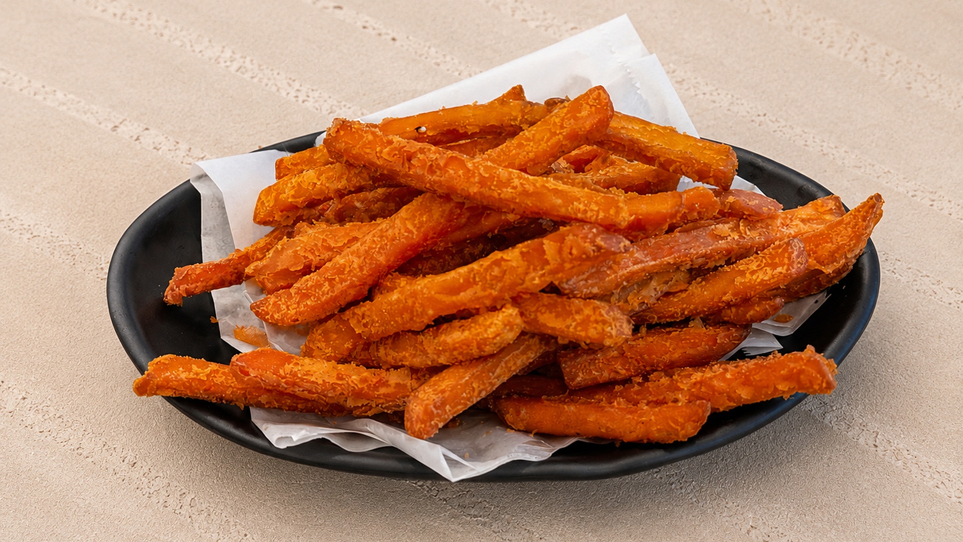 Crispy sweet potato fries on a black plate lined with paper