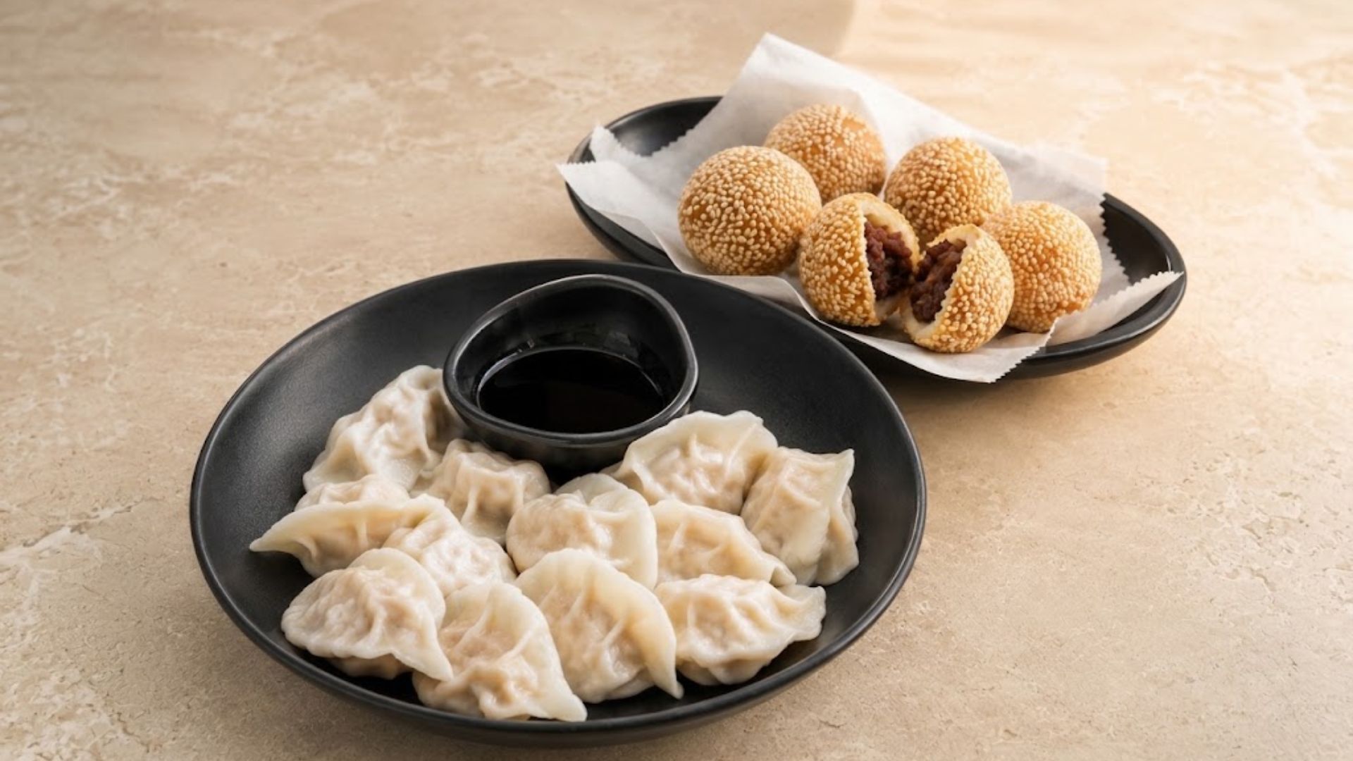 Plate of boiled dumplings with dipping sauce and a plate of red bean sesame balls