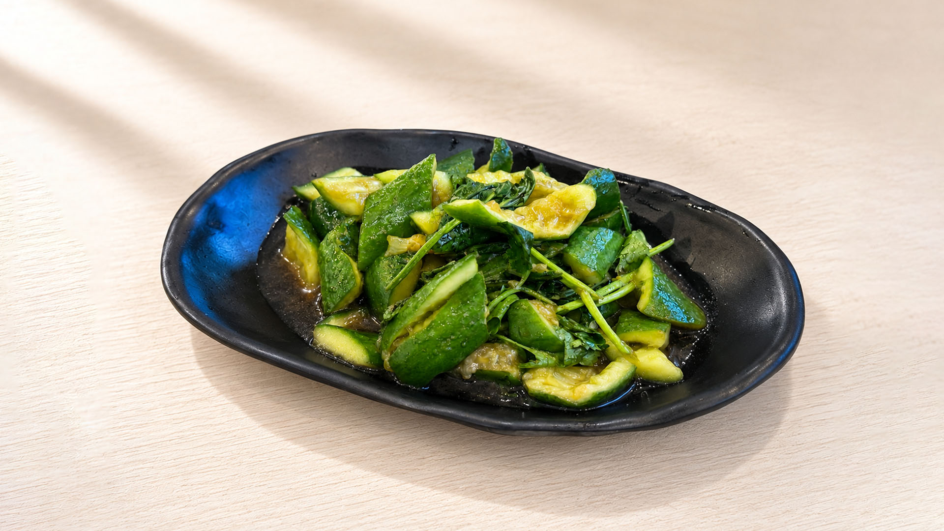 Smashed cucumber salad with garlic and herbs on a black oval plate