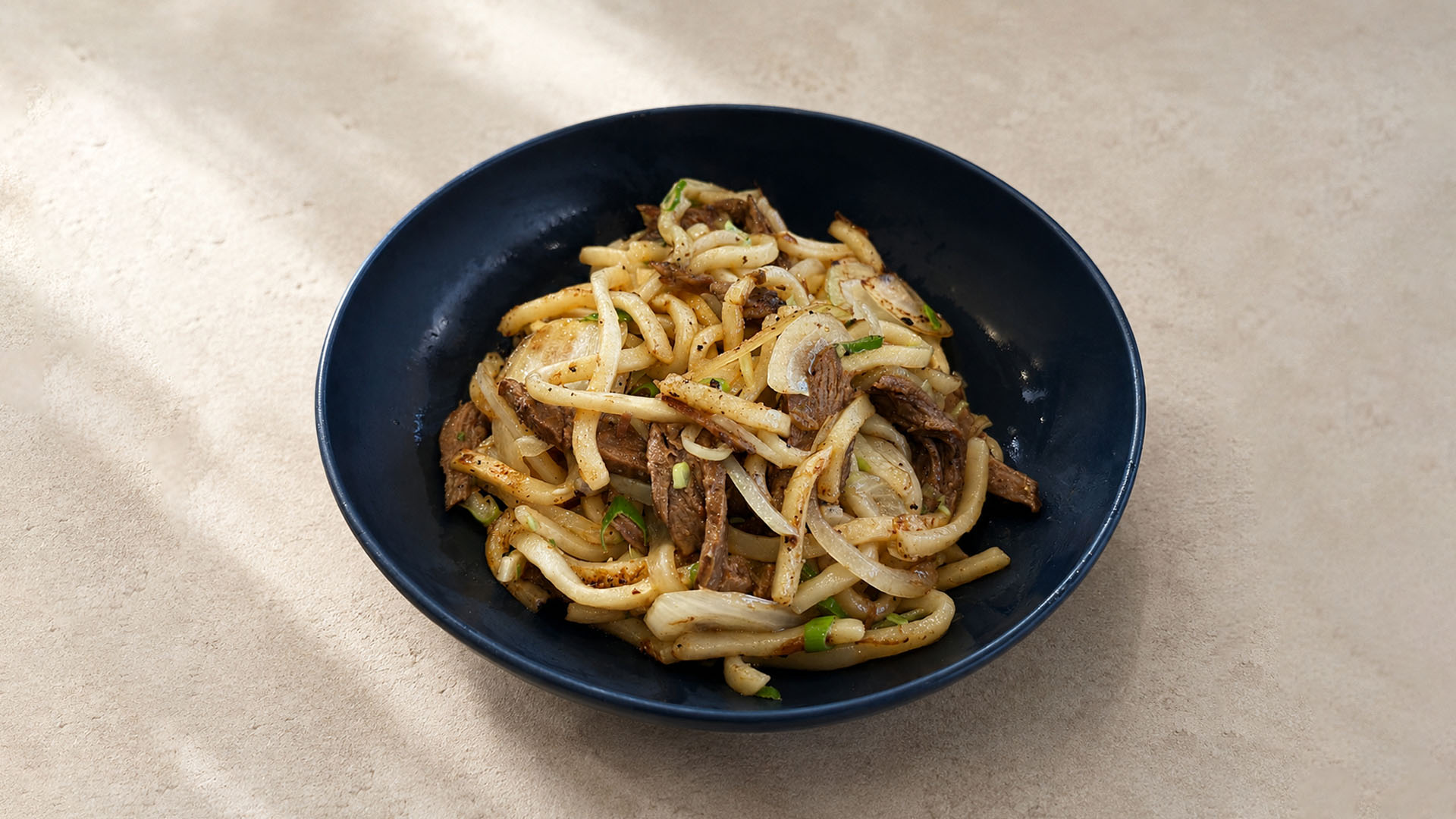 Stir-fried udon noodles with beef and onions in a black bowl