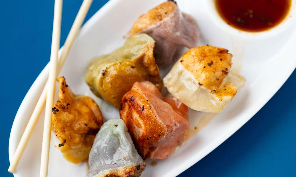 Pan-fried mixed rainbow dumplings on white plate, paired with wooden chopsticks and savory dipping sauce at Dumplings & Tea, a Asian Restaurant in Chesterfield