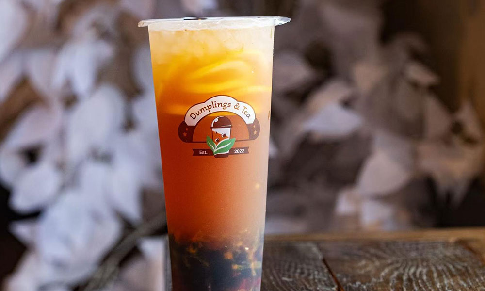 Clear plastic tall cup of fruit bubble tea featuring house Dumplings & Tea branded logo on wooden table at Dumplings & Tea, a Asian Restaurant in Chesterfield