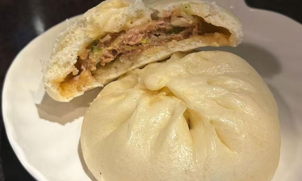 Whole steamed bun and a halved bun showing juicy pork filling placed on simple white ceramic plate at Dumplings & Tea, a Asian Restaurant in Chesterfield