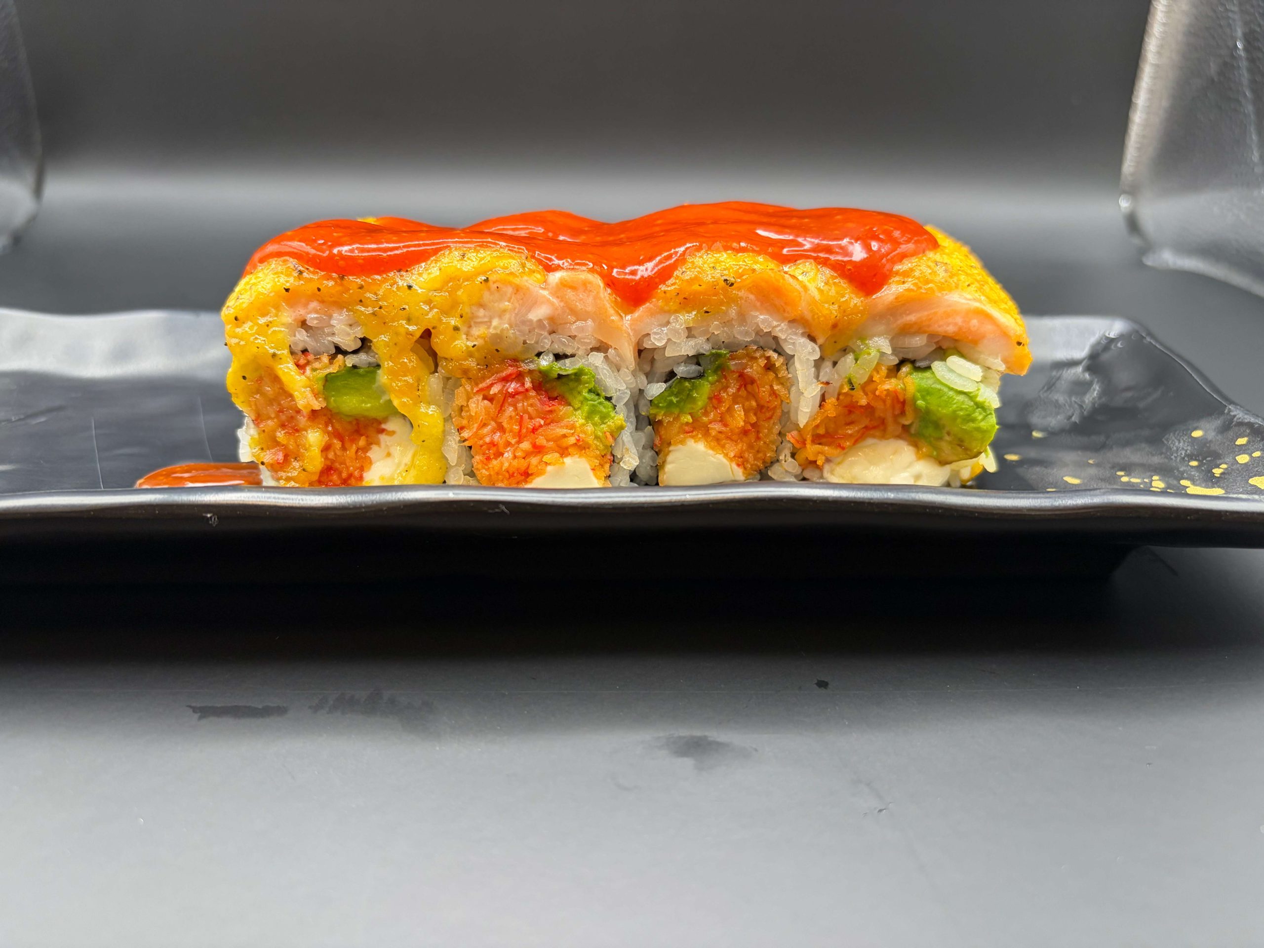 Colorful sushi roll topped with salmon, avocado, spicy sauce, and a bright red glaze