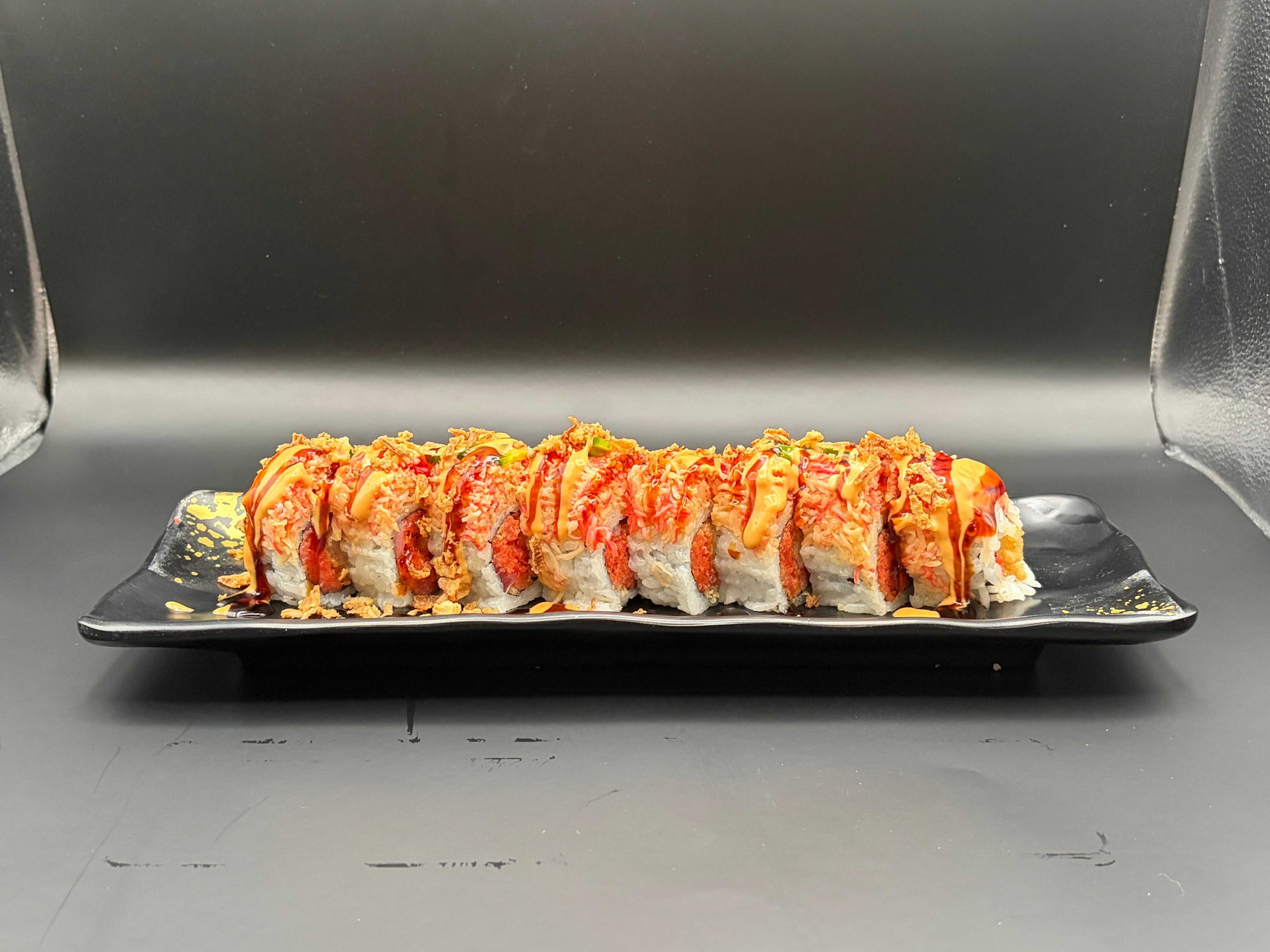 Large sushi roll topped with spicy crab mix, creamy sauce, crunchy flakes, and green onions