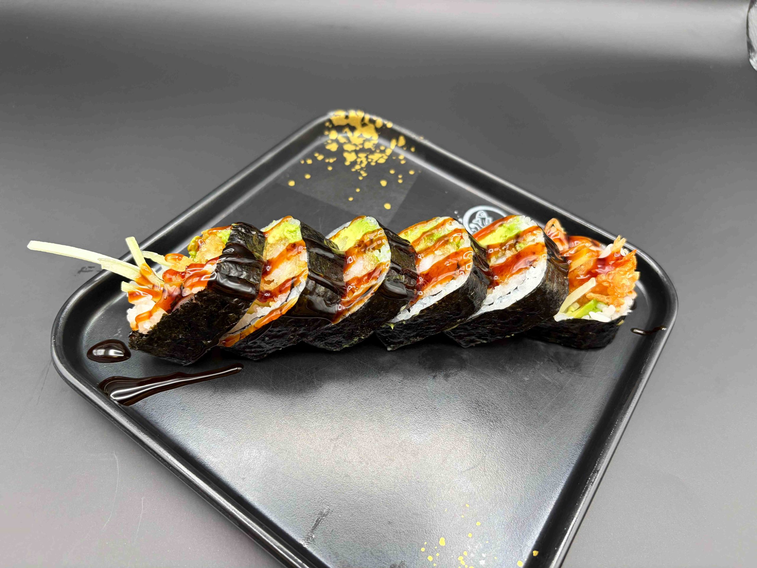 Sushi roll topped with avocado and sweet sauce, with crispy shrimp tempura inside