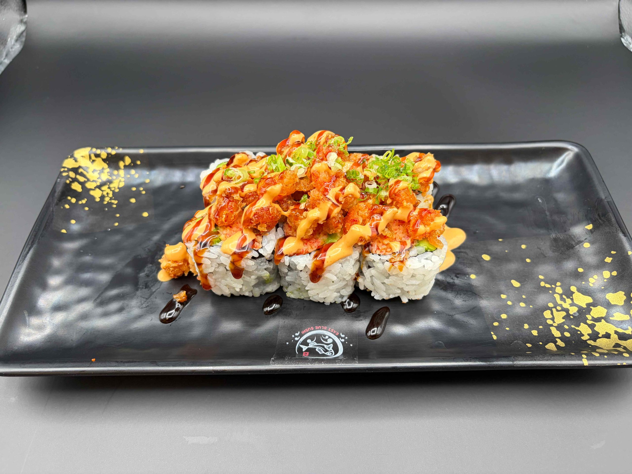 Sushi roll topped with crispy lobster bites, spicy mayo, sweet sauce, and green onions