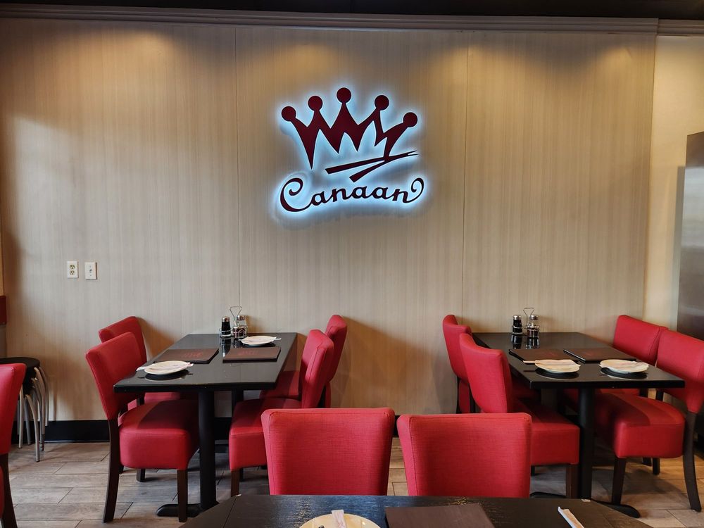 Bright red dining chairs and tables under backlit Canaan crown wall logo at Canaan Chinese Cuisine, a Chinese Restaurant in CA