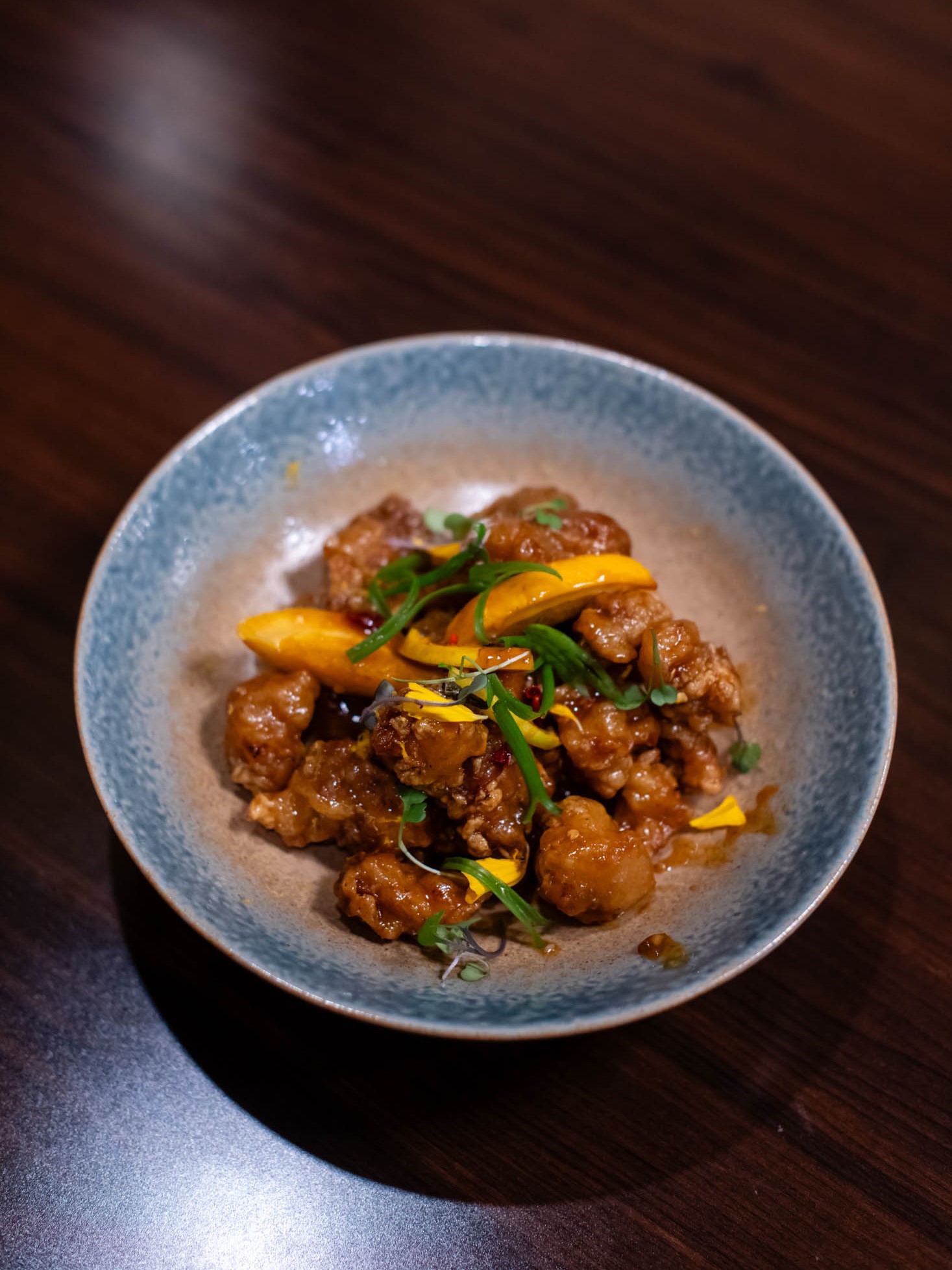 Crispy orange glazed chicken bites garnished with citrus slices and fresh herbs at Canaan Chinese Cuisine, a Chinese Restaurant in CA
