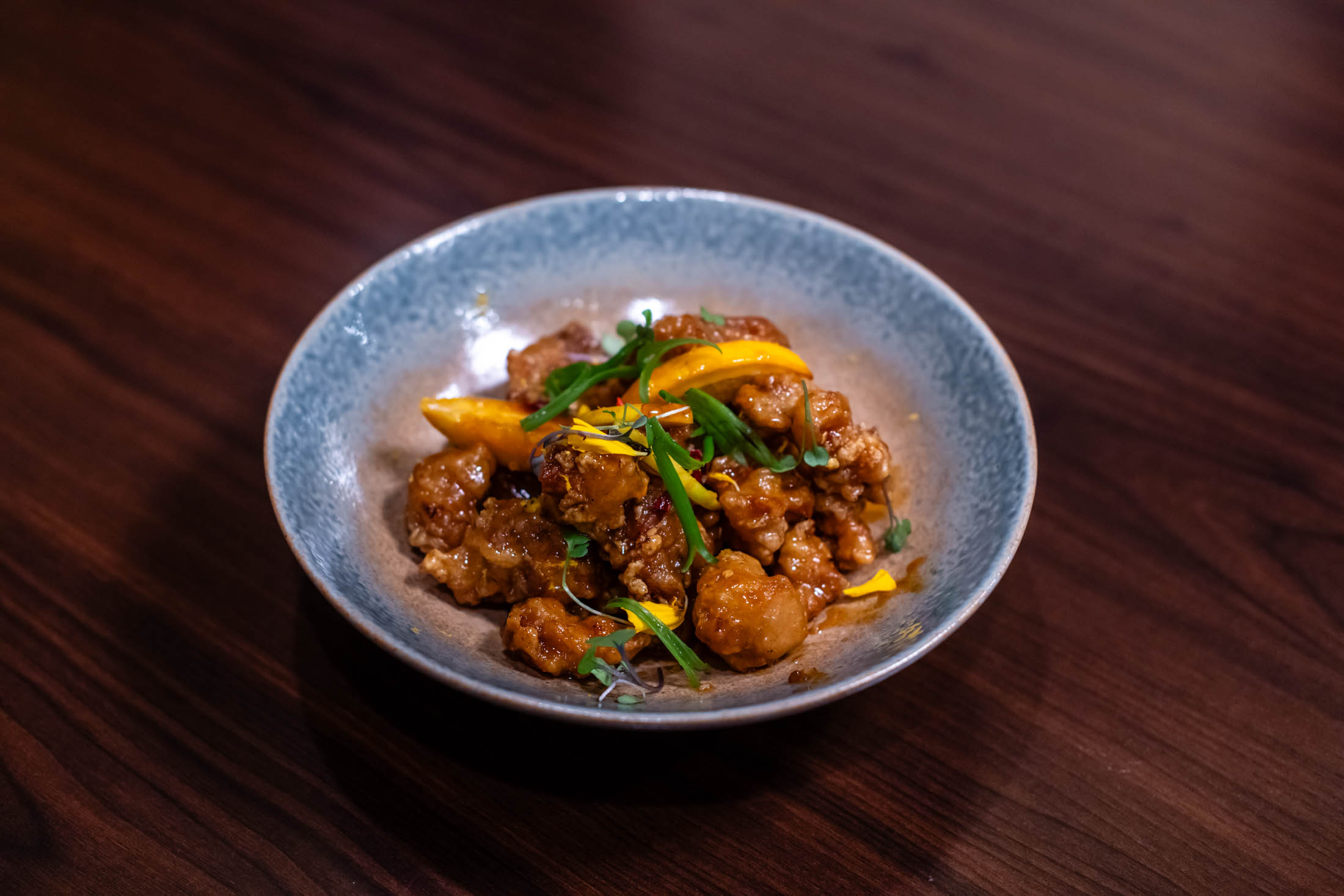 Sweet citrus fried chicken chunks topped with green onion strips and edible flower petals at Canaan Chinese Cuisine, a Chinese Restaurant in CA
