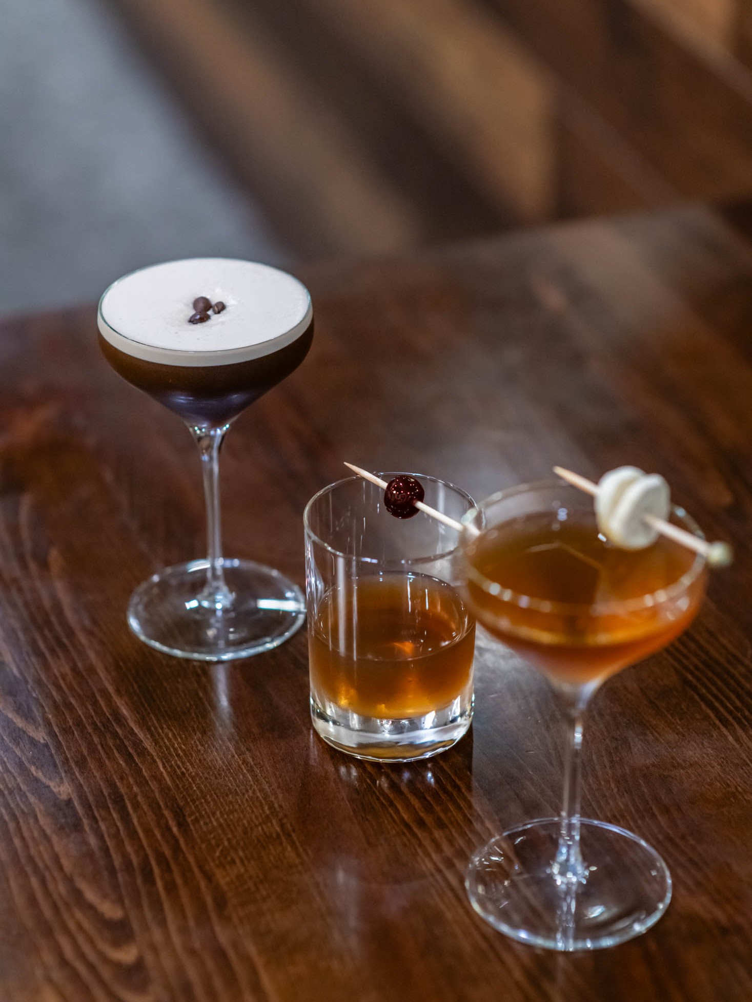 Three assorted craft cocktails with coffee bean and fruit garnishes on wood table at Canaan Chinese Cuisine, a Chinese Restaurant in CA