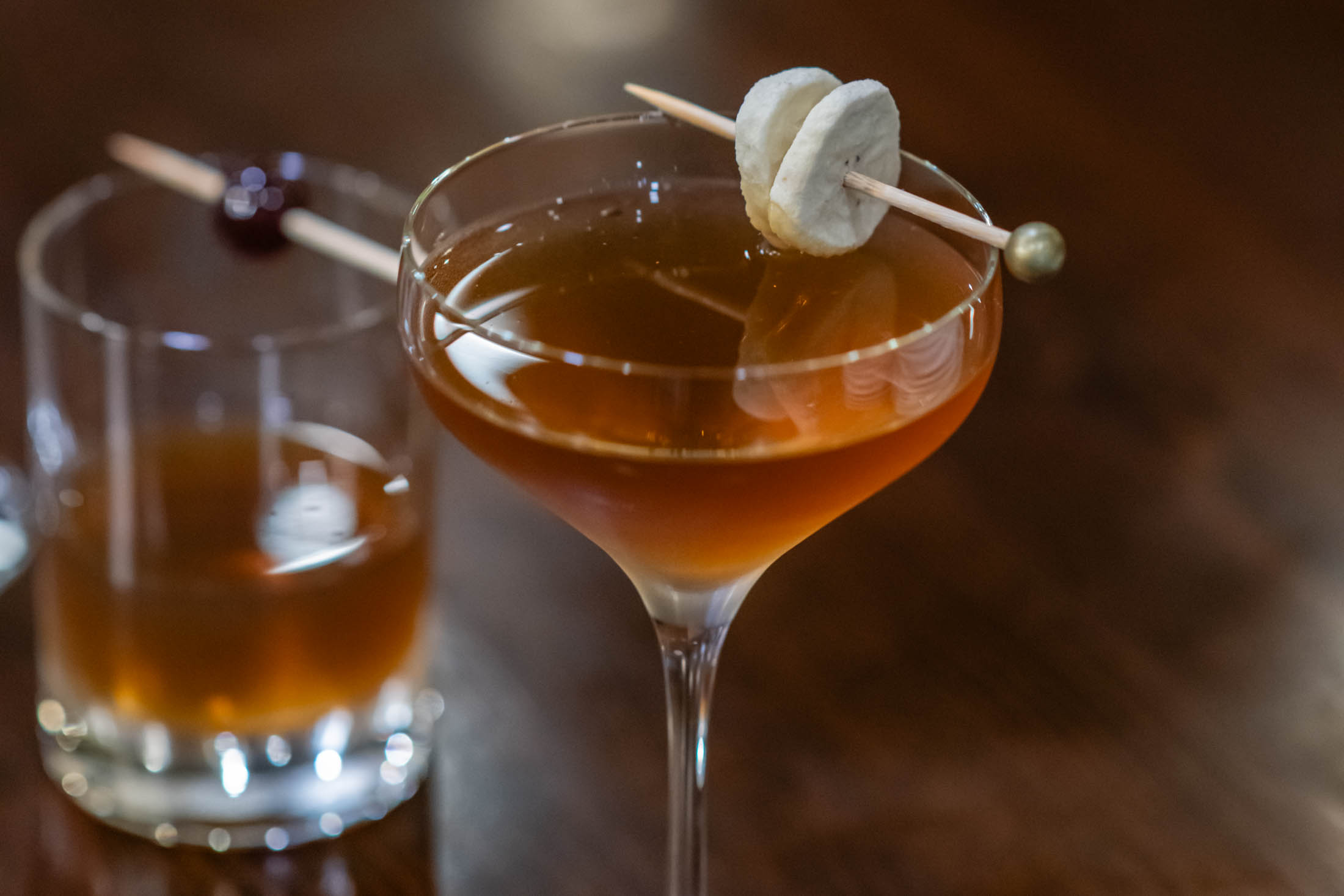 Amber craft cocktail garnished with dried banana fruit slices on wooden table at Canaan Chinese Cuisine, a Chinese Restaurant in CA