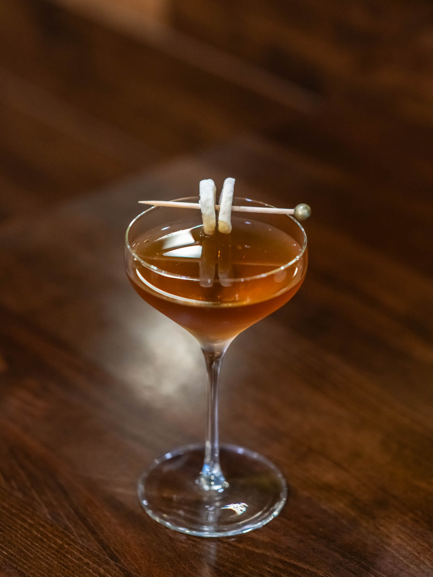 Amber martini cocktail garnished with dried banana slices on wooden table at Canaan Chinese Cuisine, a Chinese Restaurant in CA