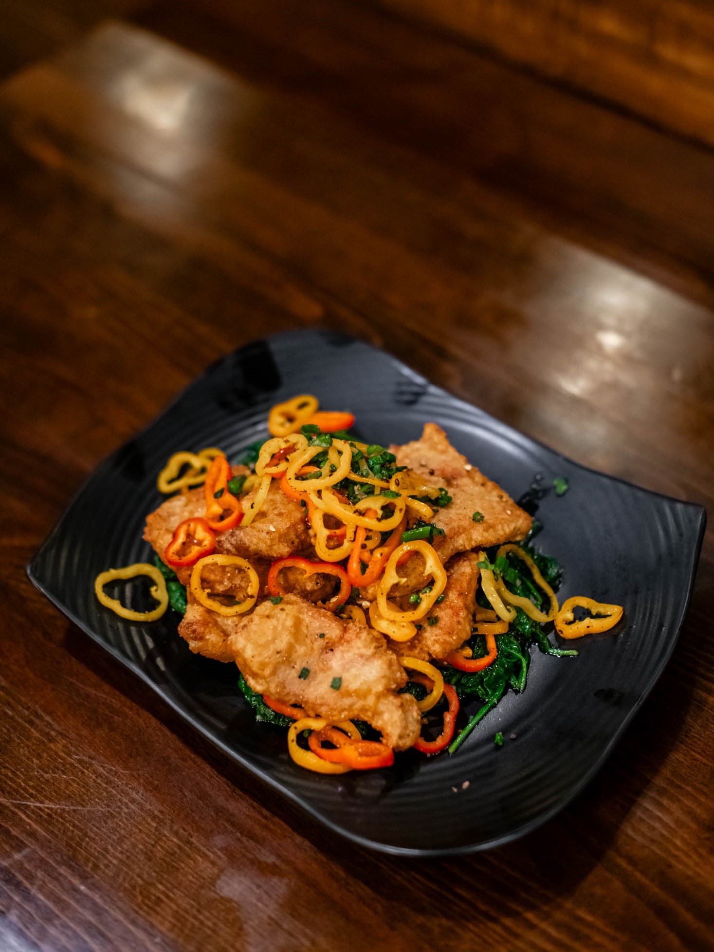 Crispy fried fish fillets topped with thin colorful bell pepper rings over greens at Canaan Chinese Cuisine, a Chinese Restaurant in CA