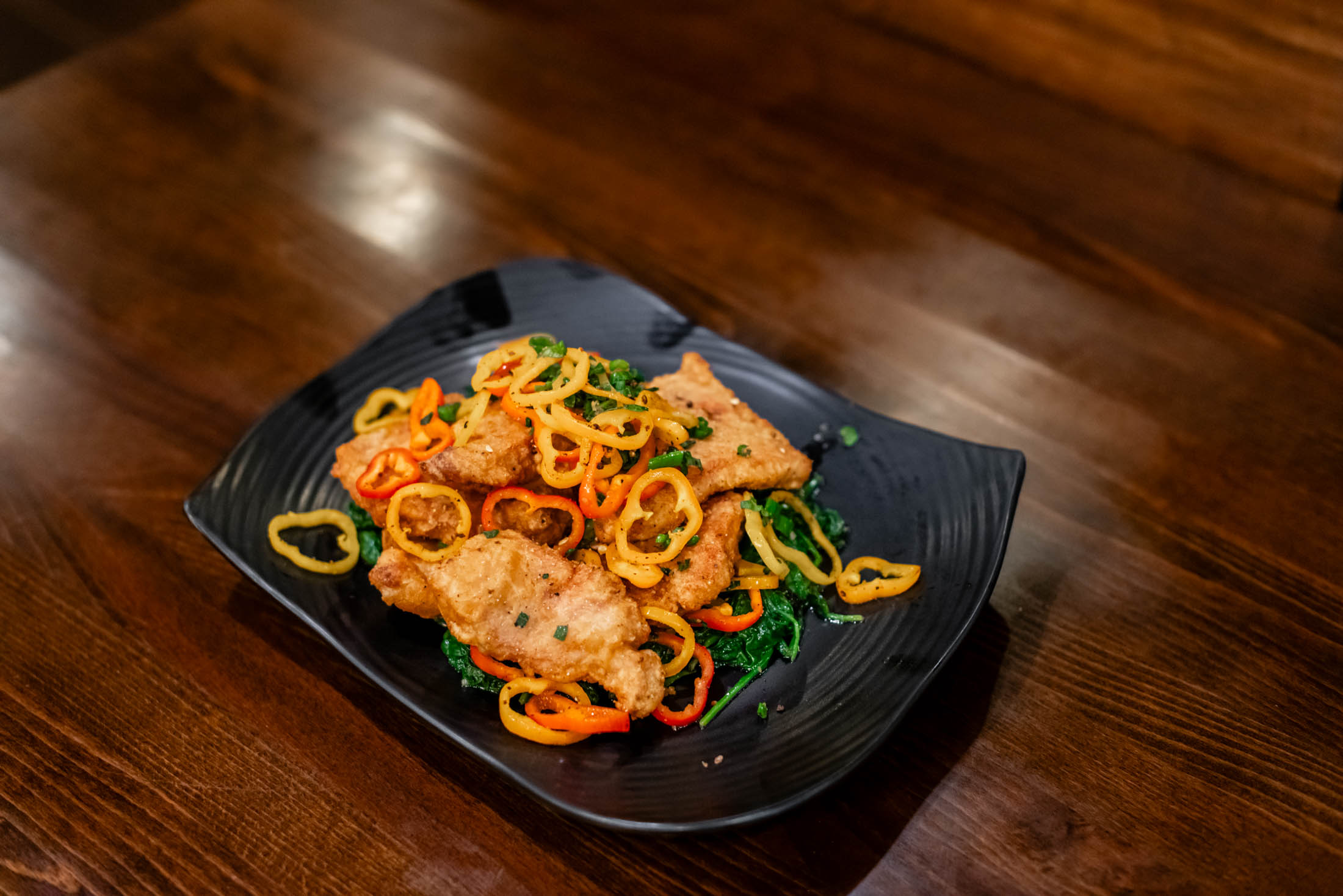 Crispy fried fish fillets topped with colorful thin bell pepper rings over greens at Canaan Chinese Cuisine, a Chinese Restaurant in CA