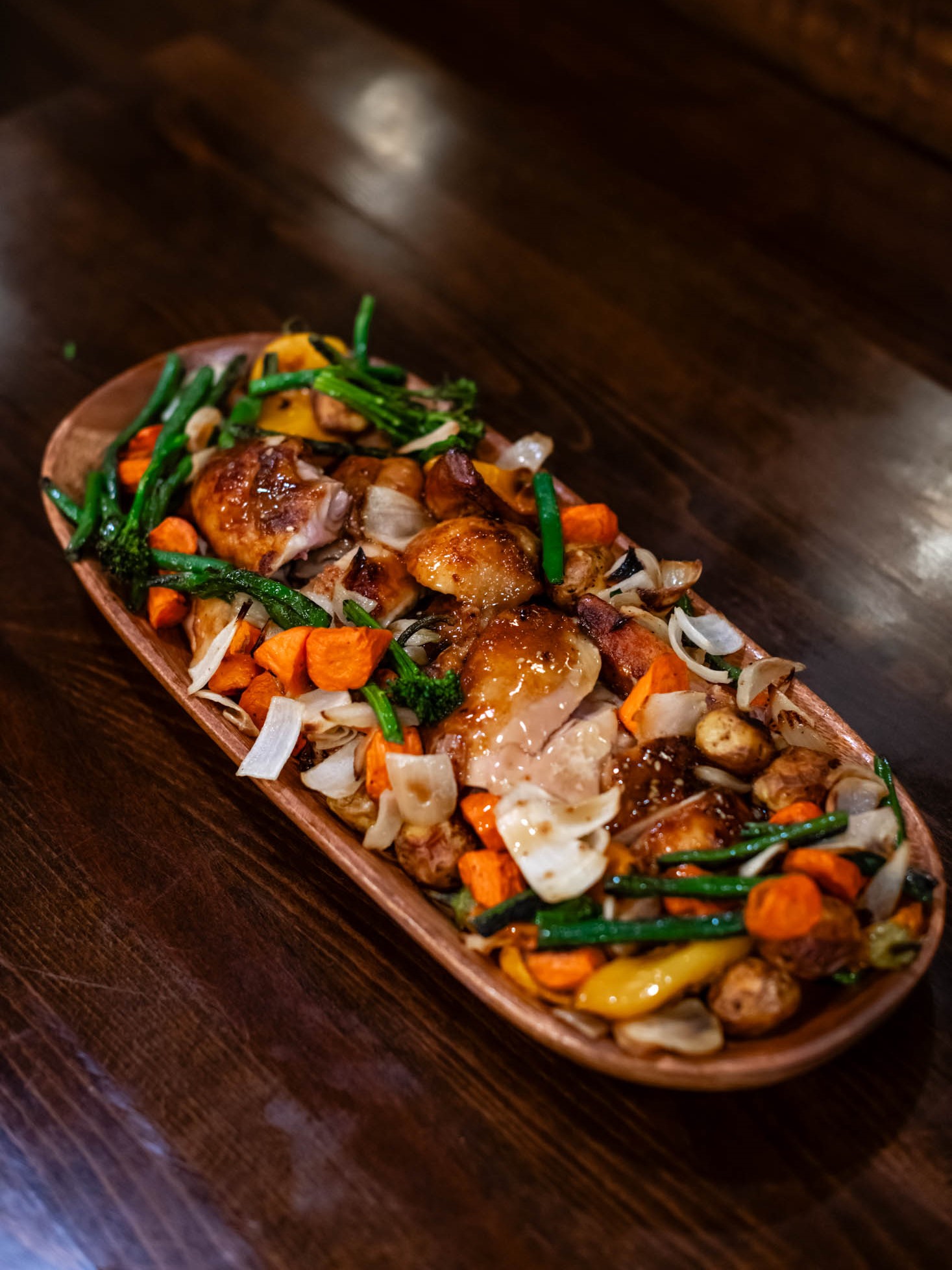 Glazed roasted chicken pieces served with mixed roasted veggies on wooden plate at Canaan Chinese Cuisine, a Chinese Restaurant in CA
