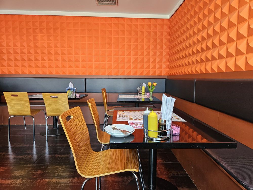Orange textured geometric wall with booth seating and light wood dining chairs at Canaan Chinese Cuisine, a Chinese Restaurant in CA