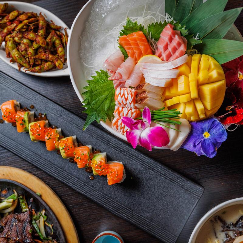 Sashimi platter with salmon, tuna, mango, and flowers; ikura rolls and edamame on side.