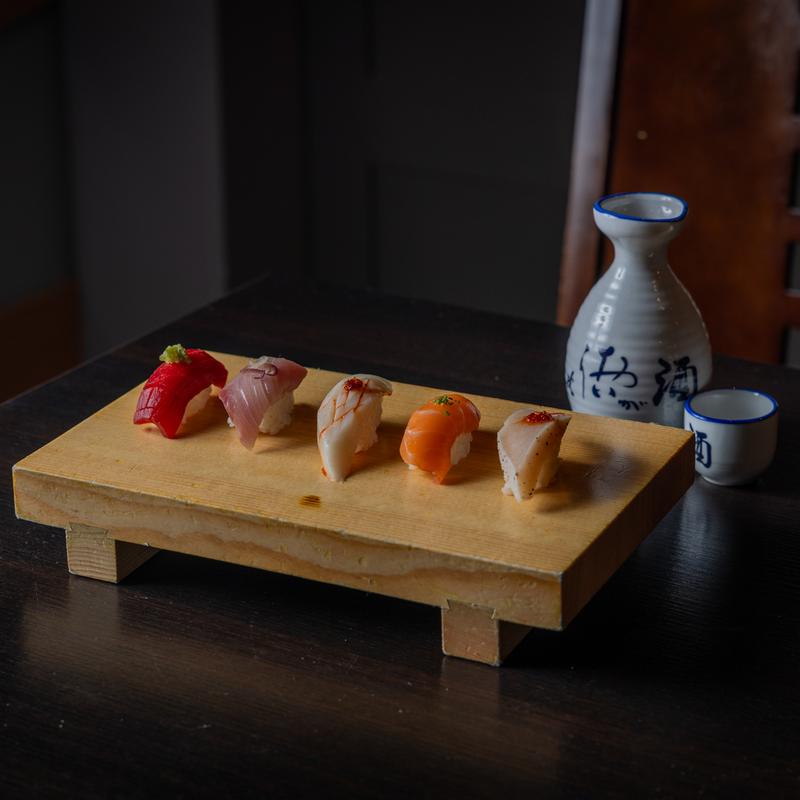 Five pieces of sashimi sushi rest on a dark-style, wood-grain plate.