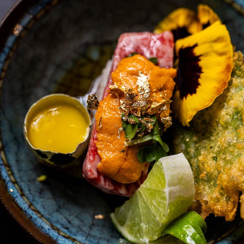 On a black plate sits a piece of tuna sushi topped with fish roe.