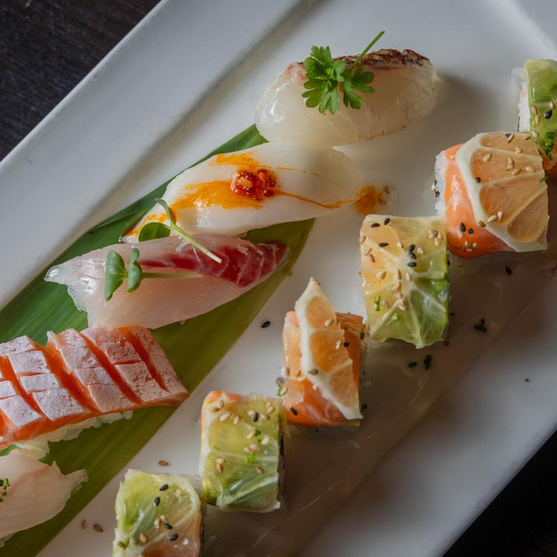 A white plate holds many pieces of sashimi and sushi.