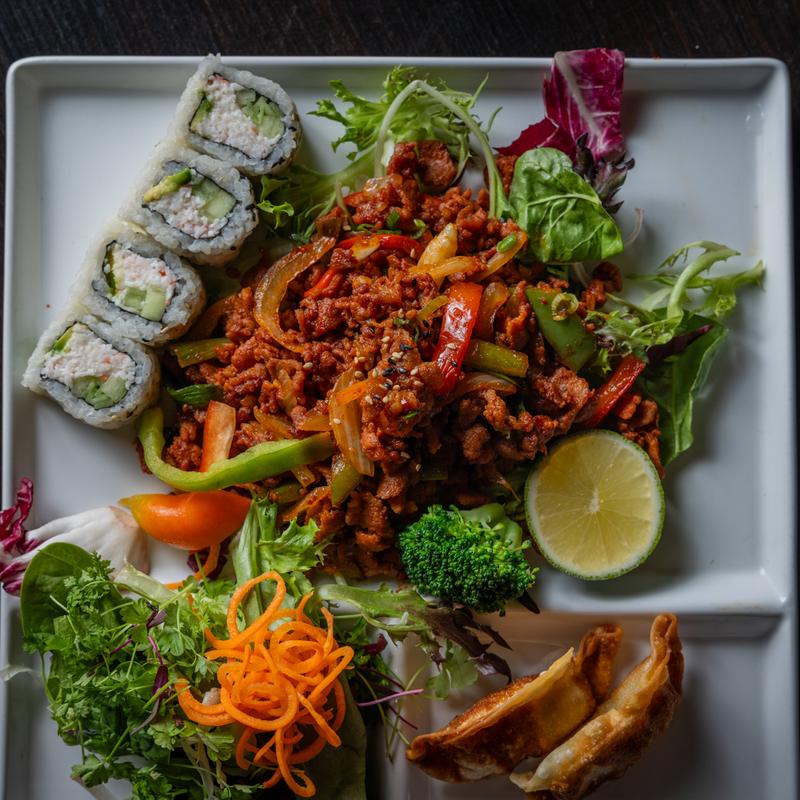 A white ceramic plate holds stir-fried beef and hand-pressed sushi.