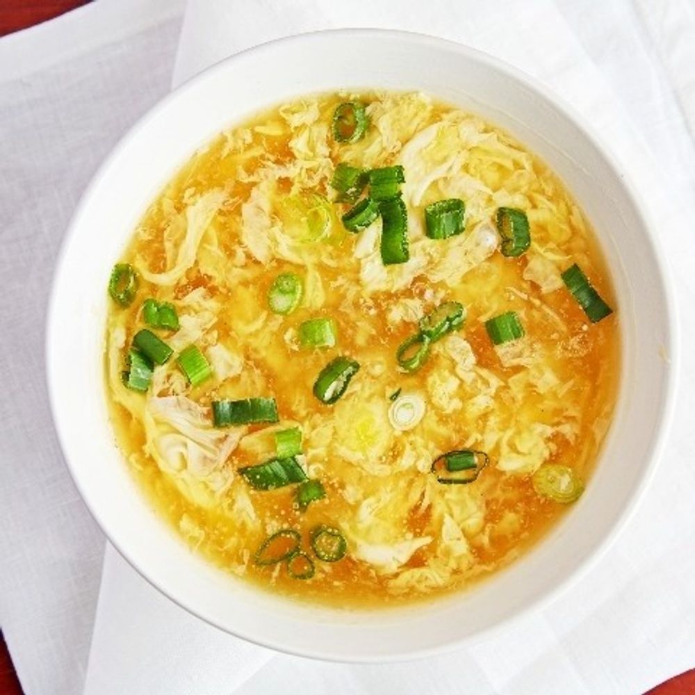 Egg drop soup with chopped scallions in a white bowl