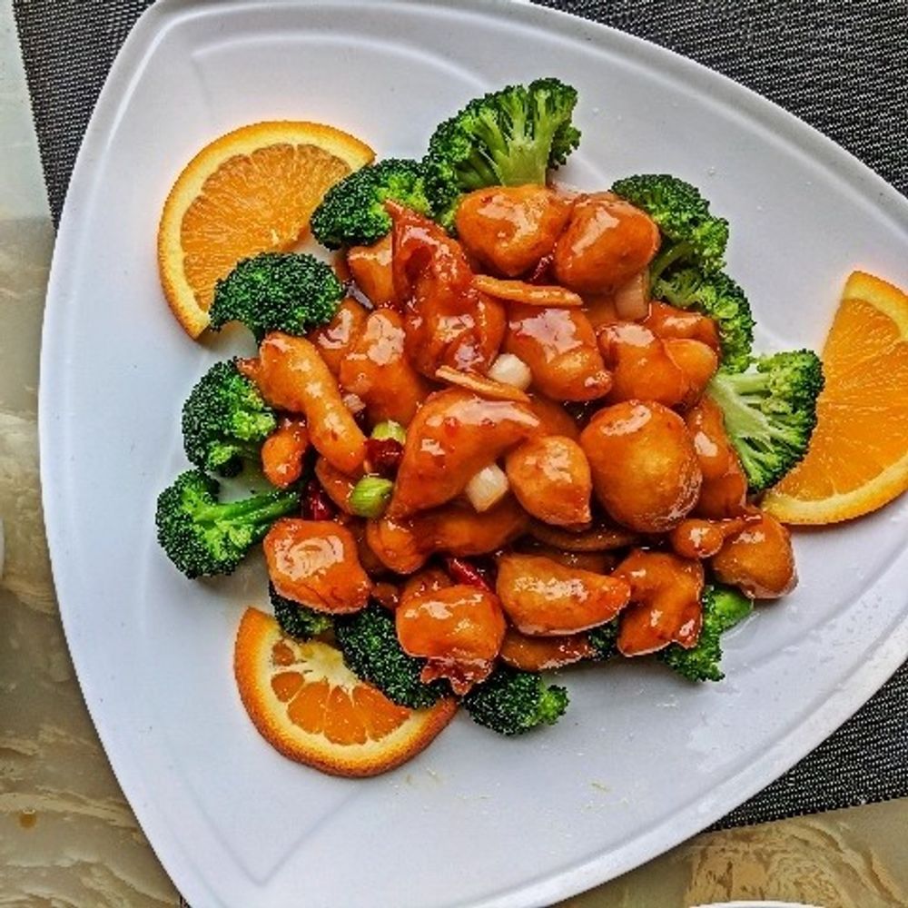 Orange chicken with broccoli and orange slices on a white plate