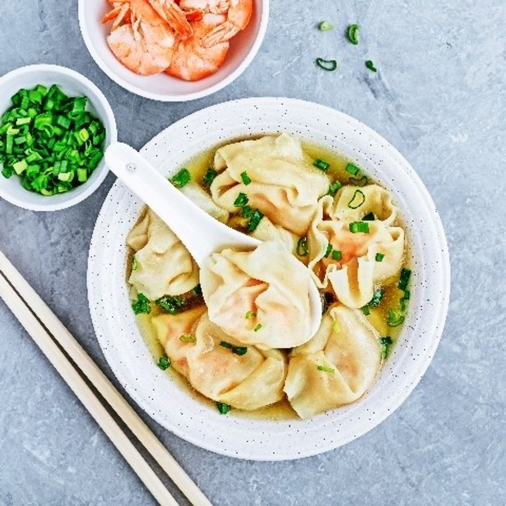 Wonton soup with scallions in a white bowl, with shrimp on the side