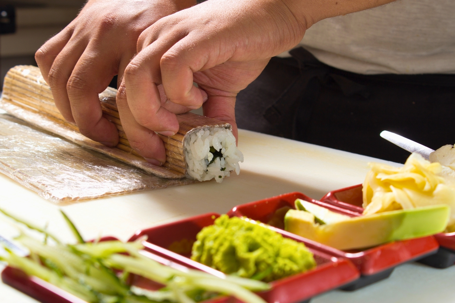 Chef rolling sushi with bamboo mat beside fresh ingredients at Elgin Buffet, a Buffet Restaurant in Elgin