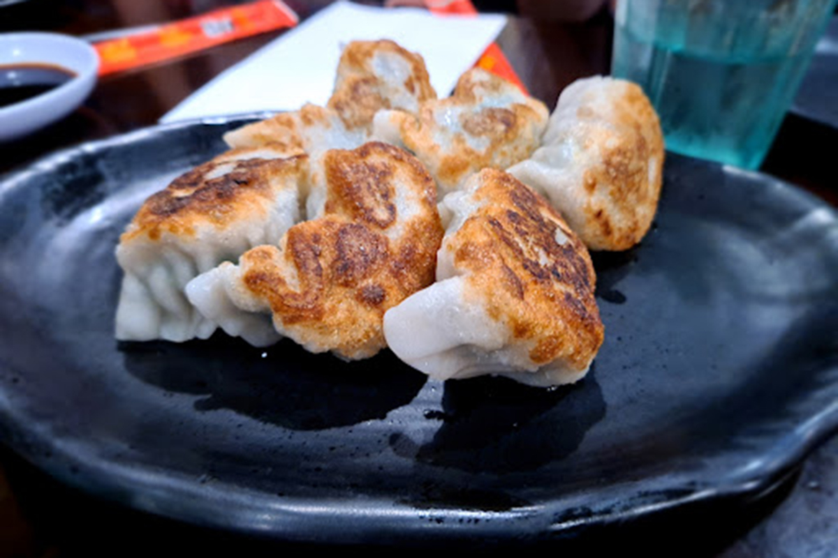 Pan-fried crispy dumplings served on glossy black ceramic plate at E Noodle Chinatown, a Chinese Restaurant in New York