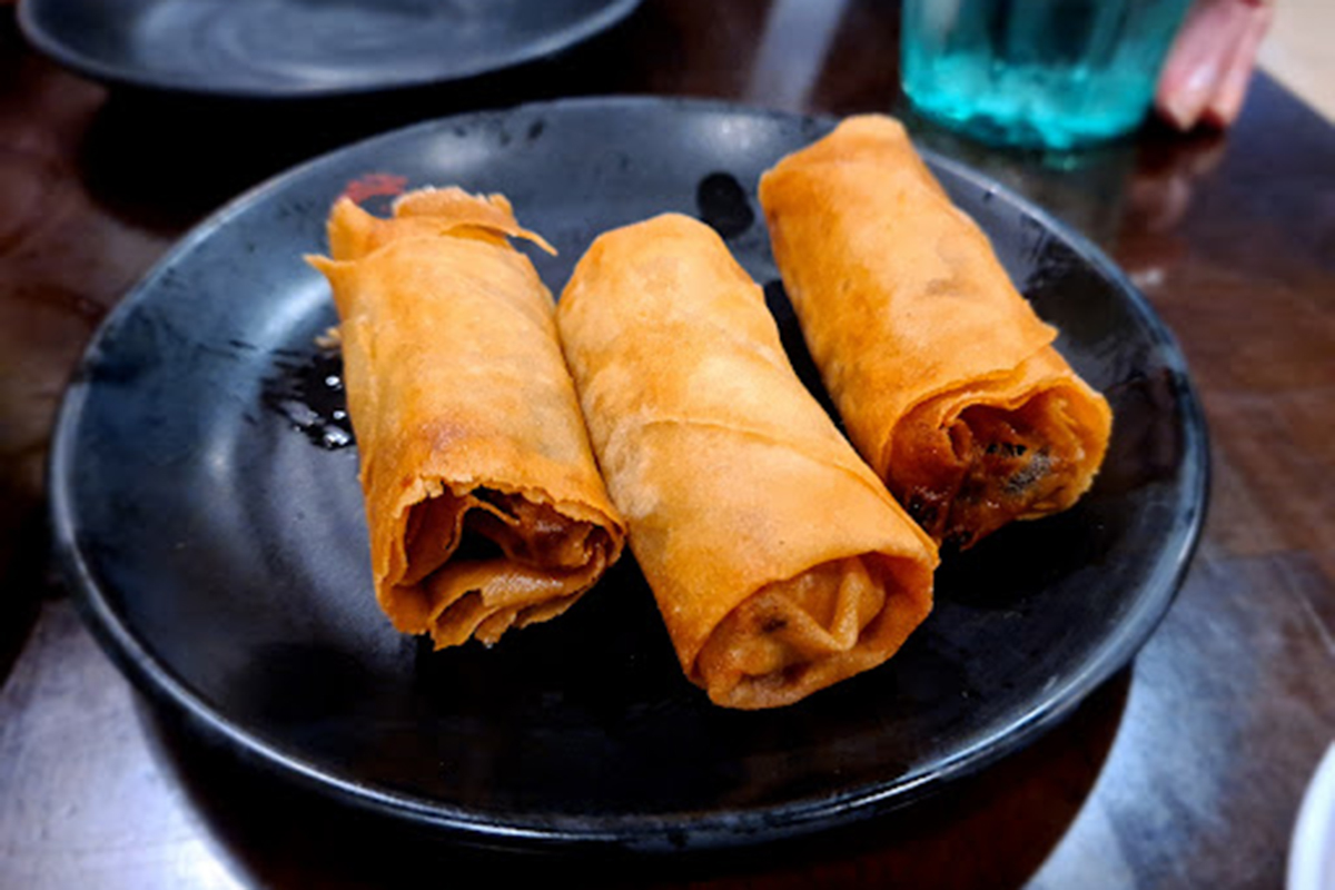 Three golden crispy vegetable spring rolls on black round plate at E Noodle Chinatown, a Chinese Restaurant in New York