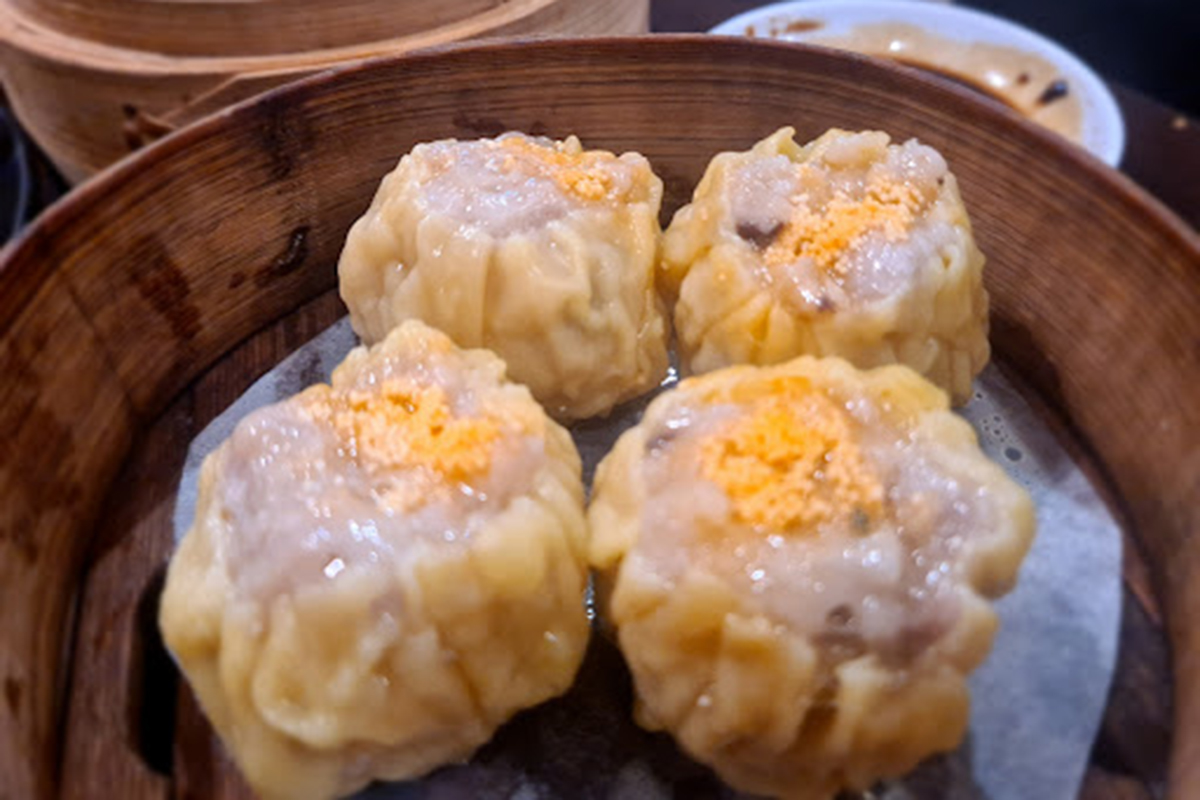 Four steamed pork siu mai topped with orange fish roe in bamboo steamer at E Noodle Chinatown, a Chinese Restaurant in New York