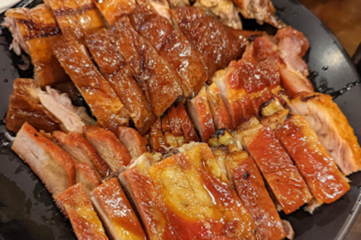 Sliced crispy roast duck platter with glossy golden skin on black ceramic plate at E Noodle Chinatown, a Chinese Restaurant in New York